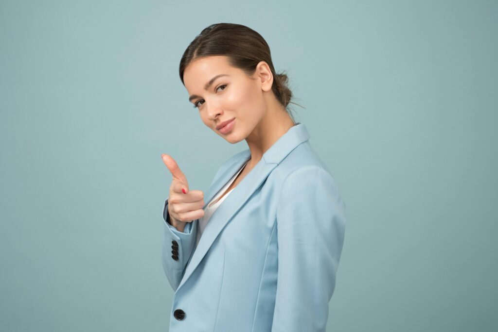 A young woman in a blue suit exhibits confidence with a relaxed pose against a blue background.